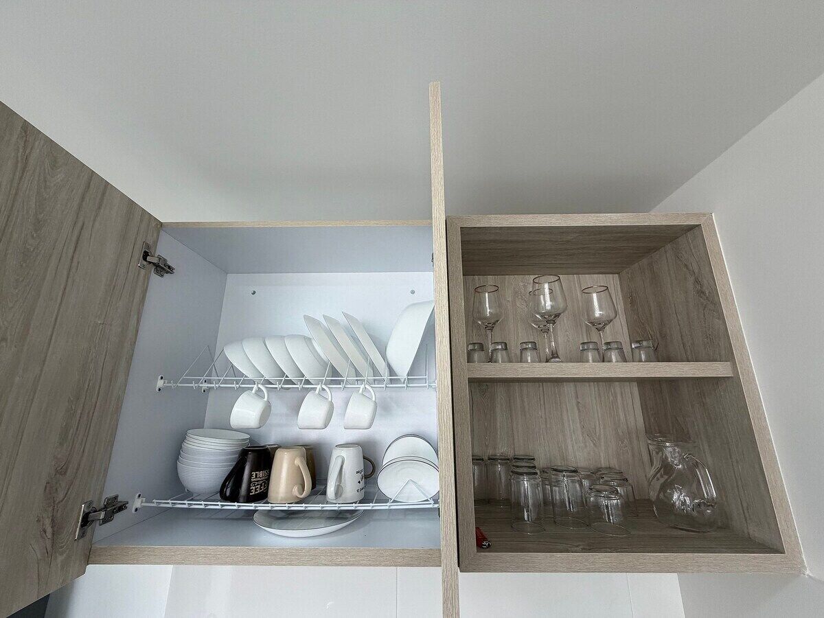 A kitchen cabinet with shelves holding dishes, cups, and glasses.