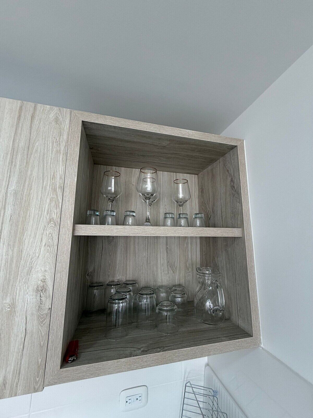 Ein Holzkabinent mit zwei Ablagen, eine mit Weingläsern und die andere mit Glasbehältern.