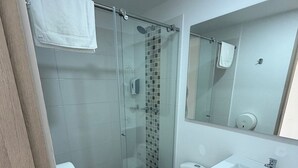 A modern bathroom with a glass-enclosed shower, a toilet, a sink, and a mirror. - Sophisticated & Spacious | Prime Location (Manizales)