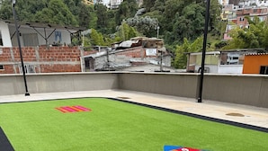 Un área de césped artificial verde con un juego de rayuela colorido y una pista de atletismo negra.