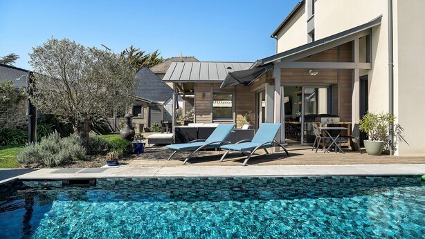 Una piscina con sillones, un área de patio y una casa de diseño moderno.