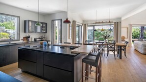 Cocina moderna con una isla grande, comedor con sillas y ventanas amplias con vistas.