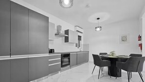 Een moderne keuken met een marmeren aanrechtblad, inbouwapparatuur en een eethoek met een ronde tafel en stoelen.