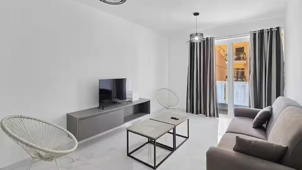 Een moderne woonkamer met een bank, een fauteuil, een salontafel, een televisie en een schuifdeur die naar een balkon leidt.