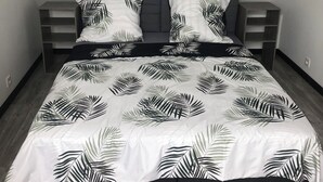 A bed with a leaf-patterned bedspread, two pillows, and a nightstand with a drawer. - Gite Eltiwen esprit bar (la croix hellean)