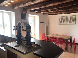 A kitchen with two beer taps, a chalkboard menu, a dining area with red chairs, and a painting on the wall.