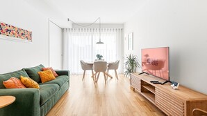 Una sala de estar moderna con un sofá verde, una mesa de comedor con sillas, un televisor y un mueble de madera.