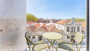 Un balcón con una mesa y sillas, con vista a un paisaje urbano que incluye edificios históricos y un cielo despejado.