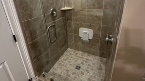 A walk-in shower with a glass door, tiled walls, a handheld showerhead, a handheld shower, a handheld shower control, a towel dispenser, and a floor drain. - Cozy 2-bedroom villa in marvelous Fort Myers with AC (Fort Myers)