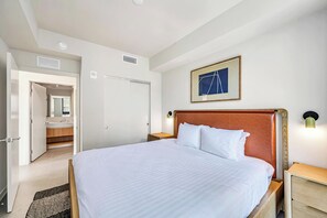 Ein Hotelzimmer mit einem Bett, einem Nachttisch, einer Wandlampe, einem gerahmten Bild und einem sichtbaren Badezimmer durch eine offene Tür.