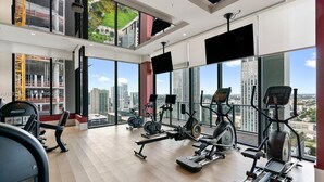 A gym with cardio machines, weight equipment, and large windows offering a city view. - The Crosby (Miami)