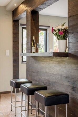 A bar area with two stools, a wine bottle, and a vase with flowers. - Aroeira Pool House by lisbon-coast vacation (Charneca da Caparica)