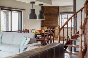 A modern living room with a sofa, dining table, and chairs. A wooden staircase with a railing is visible. - Aroeira Pool House by lisbon-coast vacation (Charneca da Caparica)