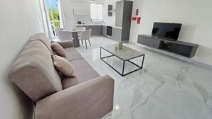 Ein modernes Wohnzimmer mit einer Couch, einem Couchtisch, einem Fernseher und einer Küchenzeile.