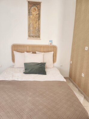 A bed with a headboard, pillows, a quilt, and a wall-mounted painting. - Cosy apartment (Nîmes)