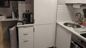 Ett kompakt kök med en kaffemaskin, en diskho och en papperskorg.
