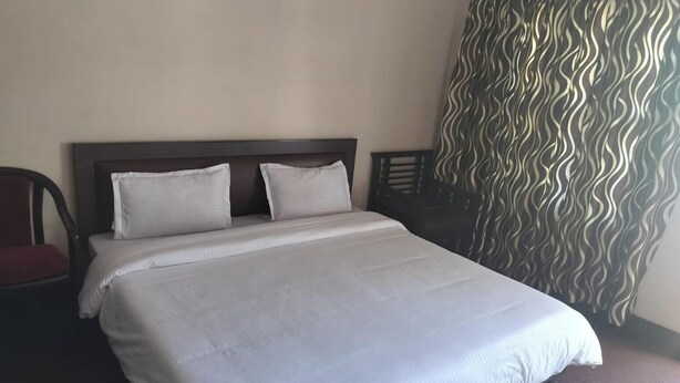 A hotel room with a bed, two pillows, a chair, and a curtain with a wavy pattern. - Saalak Lite Social Palace  (Ukhimath)