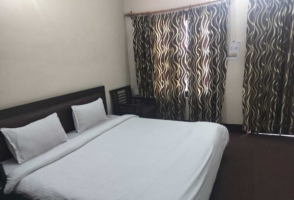 A hotel room with a large bed, a wooden headboard, a desk, and a patterned curtain.