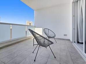 Un balcon avec deux chaises en métal, un sol carrelé et une vue sur des bâtiments au loin.
