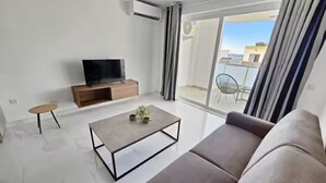 Ein modernes Wohnzimmer mit einer Couch, einem Couchtisch, einem Fernseher und einer Schiebetür zu einem Außenbereich.