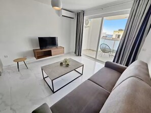 A modern living room with a sofa, a coffee table, a TV, and a sliding glass door leading to an outdoor area. - Large terrace, centrally located modern apartment (San Pawl il-Baħar)