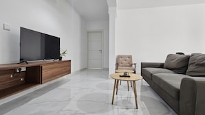 Ein modernes Wohnzimmer mit Flachbildfernseher, einer Holz-Unterhaltungsecke, einem grauen Sofa, einem runden Couchtisch und einem beigen Sessel.