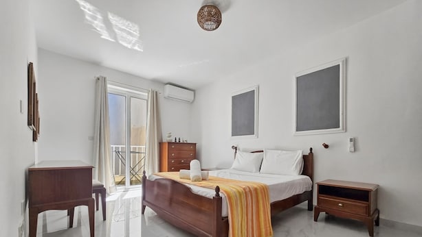 Ein Schlafzimmer mit Bett, Kommode, Nachttisch, Schreibtisch und einem Balkon.