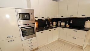 A kitchen with white cabinets, a microwave, an oven, a sink, and a black countertop. - 3 Rhodewood House (Saundersfoot)