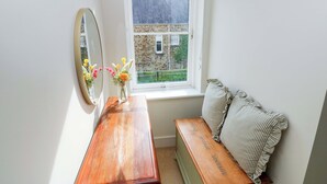 A room with a wooden bench, a mirror, and a window with a view of a stone building. - 3 Rhodewood House (Saundersfoot)