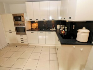 A compact kitchen with a microwave, oven, and a coffee maker. - 3 Rhodewood House (Saundersfoot)