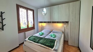 Un dormitorio con cama, ventana con cortinas, cabecero e iluminación en la pared.