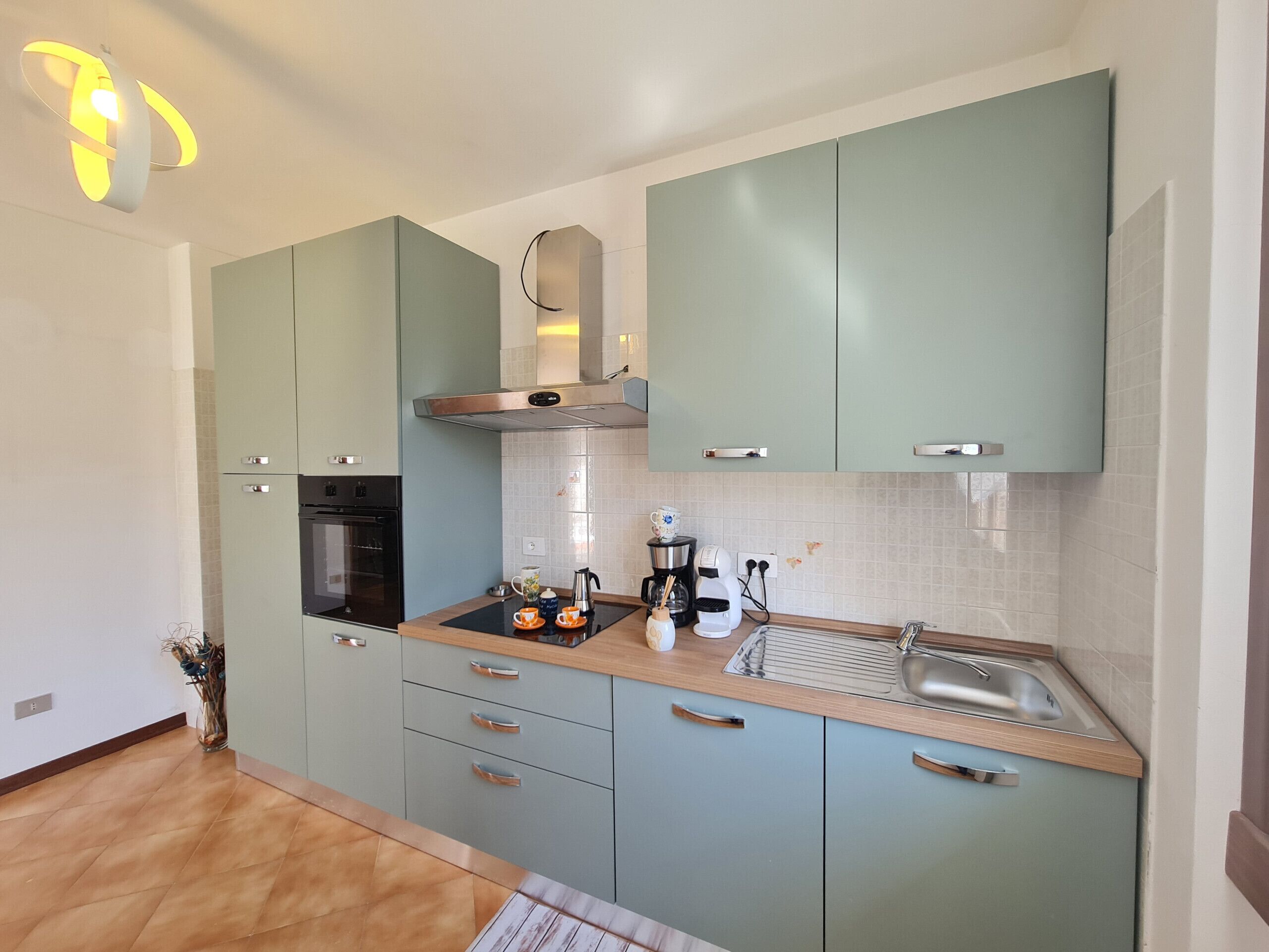 A modern kitchen with light blue cabinets, a stainless steel range hood, a built-in oven, and a wooden countertop.