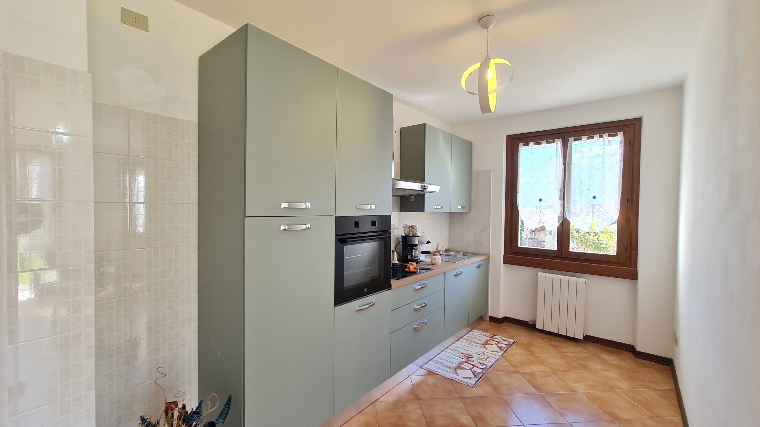 Eine Küche mit Backofen, Kaffeemaschine und einem Fenster mit Vorhängen.