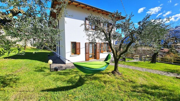 Una casa con fachada blanca, contraventanas de madera y una hamaca verde en el jardín.
