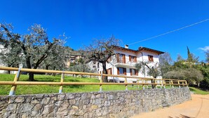 A two-story building with a stone wall in the foreground, a wooden fence, and trees in the background. - Villa La Pief - Gardasee Blick (Tremosine)