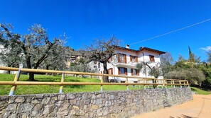 A two-story building with a stone wall in the foreground, a wooden fence, and trees in the background. - Villa La Pief - Gardasee Blick (Tremosine)