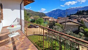 A balcony with a table and chairs, a view of a mountainous landscape, and a village below. - Villa La Pief - Gardasee Blick (Tremosine)