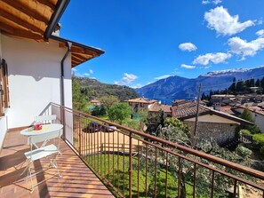 A balcony with a table and chairs, a view of a mountainous landscape, and a village below. - Villa La Pief - Gardasee Blick (Tremosine)