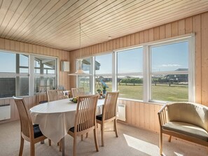 A dining area with a round table, wooden chairs, and large windows offering a view of a grassy yard. - 4 Star Holiday Home in Lokken (Lokken)