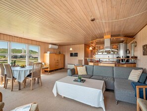 A spacious living area with a dining table, sofa, and kitchen in the background. - 4 Star Holiday Home in Lokken (Lokken)