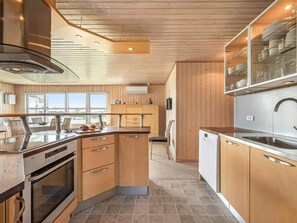 A modern kitchen with wooden cabinets, stainless steel appliances, and a large window. - 4 Star Holiday Home in Lokken (Lokken)