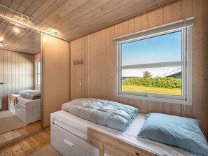 Een slaapkamer met een bed, een raam met uitzicht op een tuin en houten wanden.