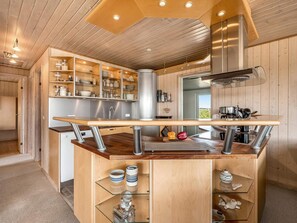 A modern kitchen with wooden cabinets, a stainless steel range hood, and a central island with a sink. - 4 Star Holiday Home in Lokken (Lokken)