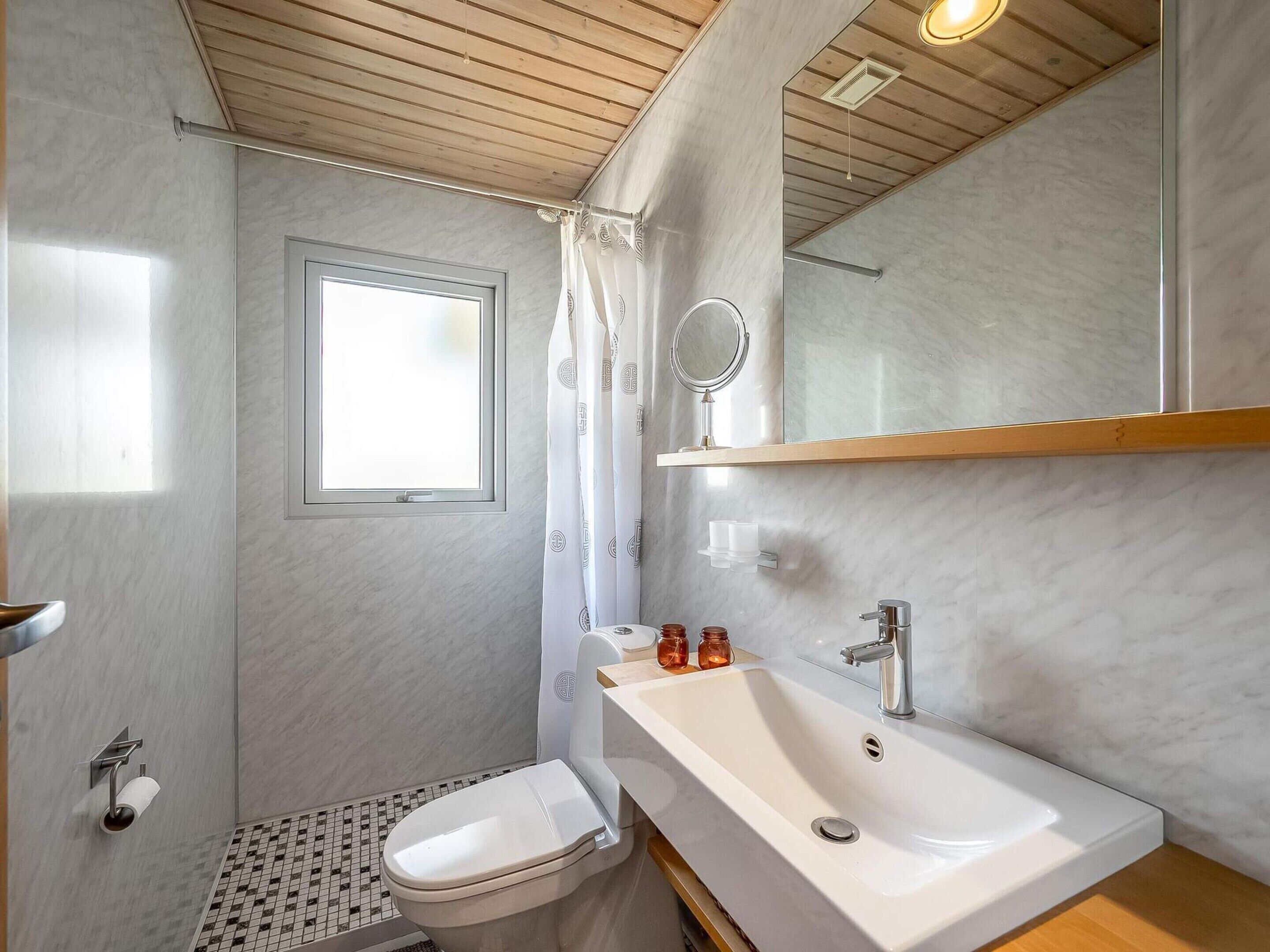 Et badeværelse med toilet, vask, spejl og bruseforhæng.