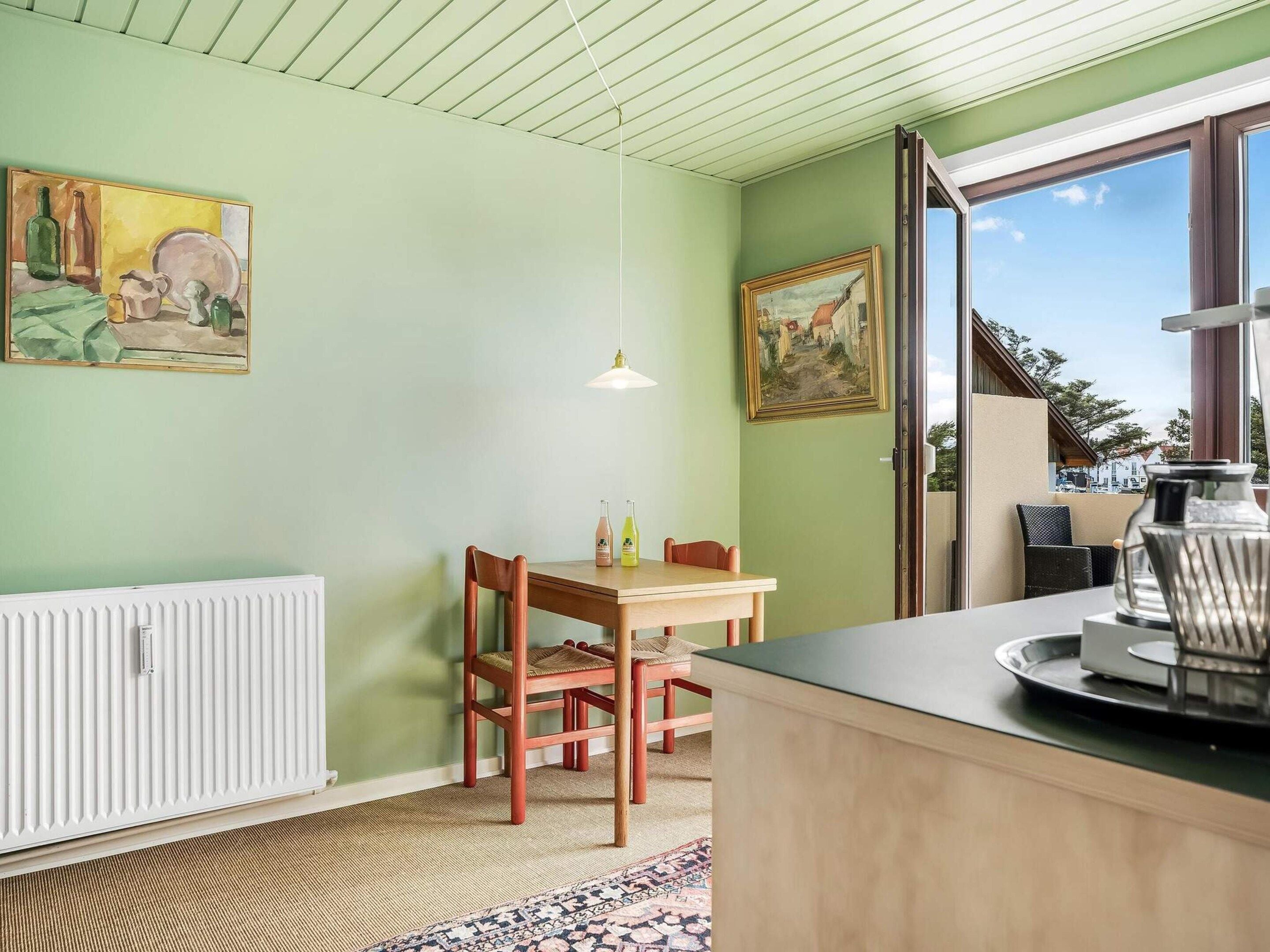 Une pièce comprenant une table à manger, des chaises, un radiateur, un tableau et une fenêtre donnant sur un paysage.