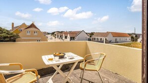 A balcony with a table and chairs, overlooking a street with houses and a clear sky. - 4 Star Holiday Home in Lokken (Lokken)
