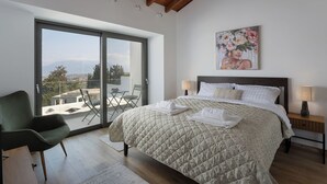Une chambre à coucher comprenant un lit, une chaise, une table de chevet, un tableau et une vue sur l’extérieur, accessible par une porte coulissante.