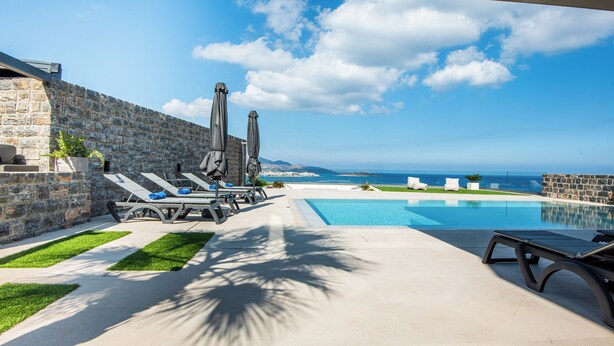 Ein Poolbereich mit Liegestühlen, Sonnenschirmen und Blick aufs Meer.