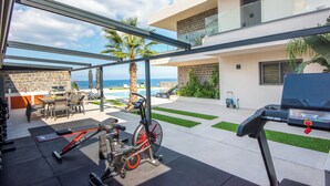 Eine moderne Außenpatio mit Fitnessgeräten, einem Grill und Blick aufs Meer.