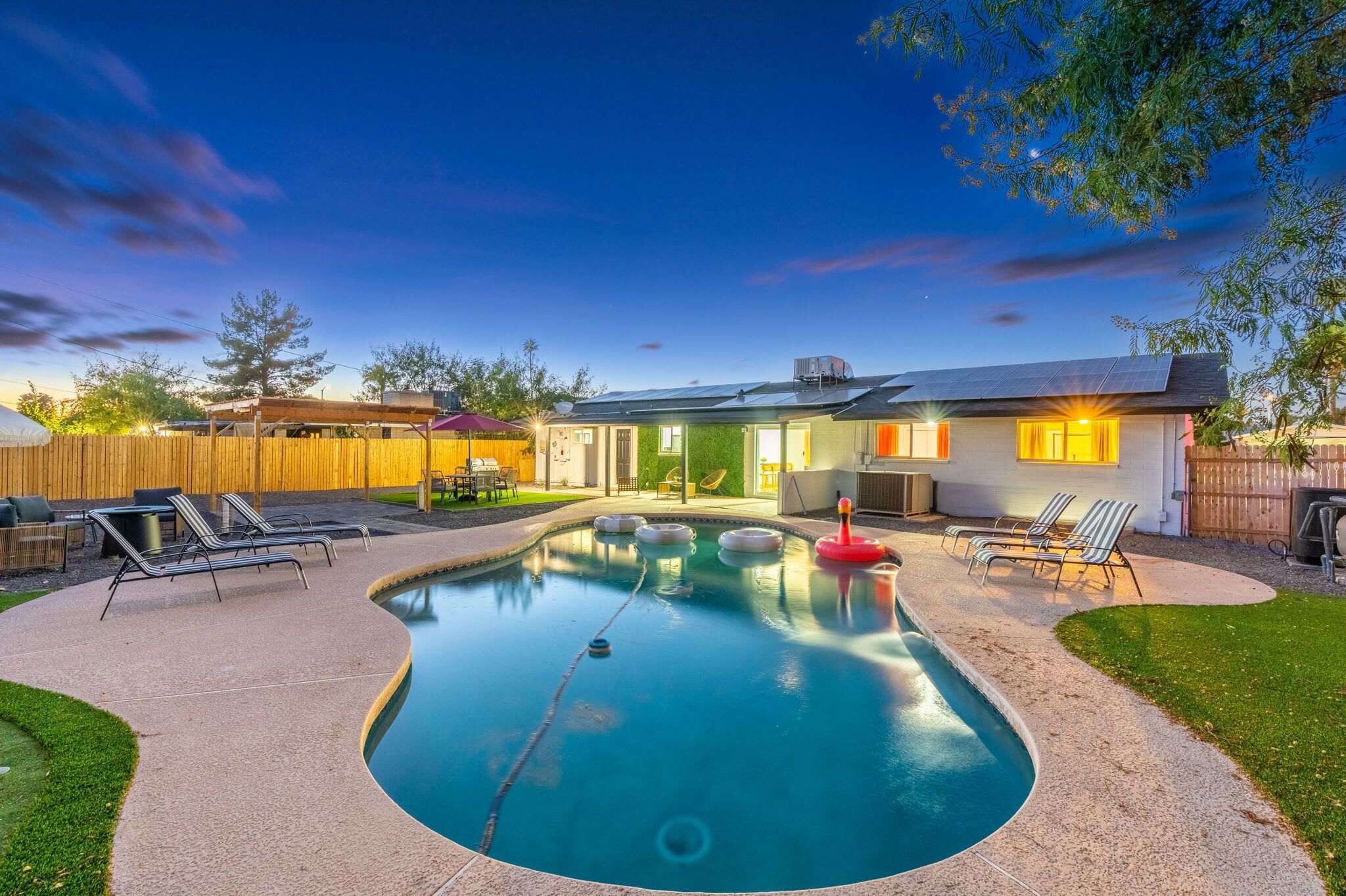 A backyard with a swimming pool, lounge chairs, and a house with a solar panel.